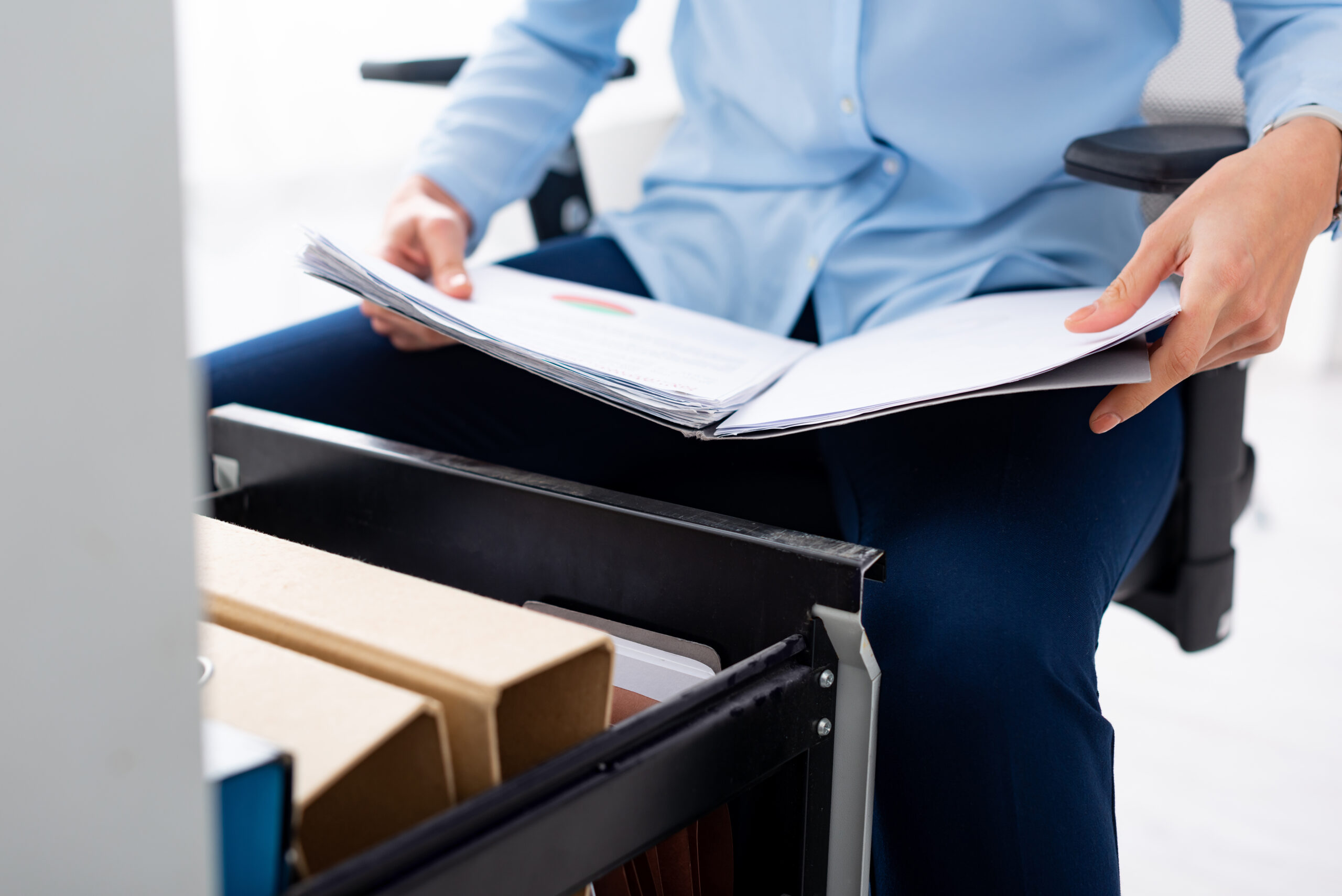 Cropped view of businesswoman holding folder with papers near open cabinet driver on white