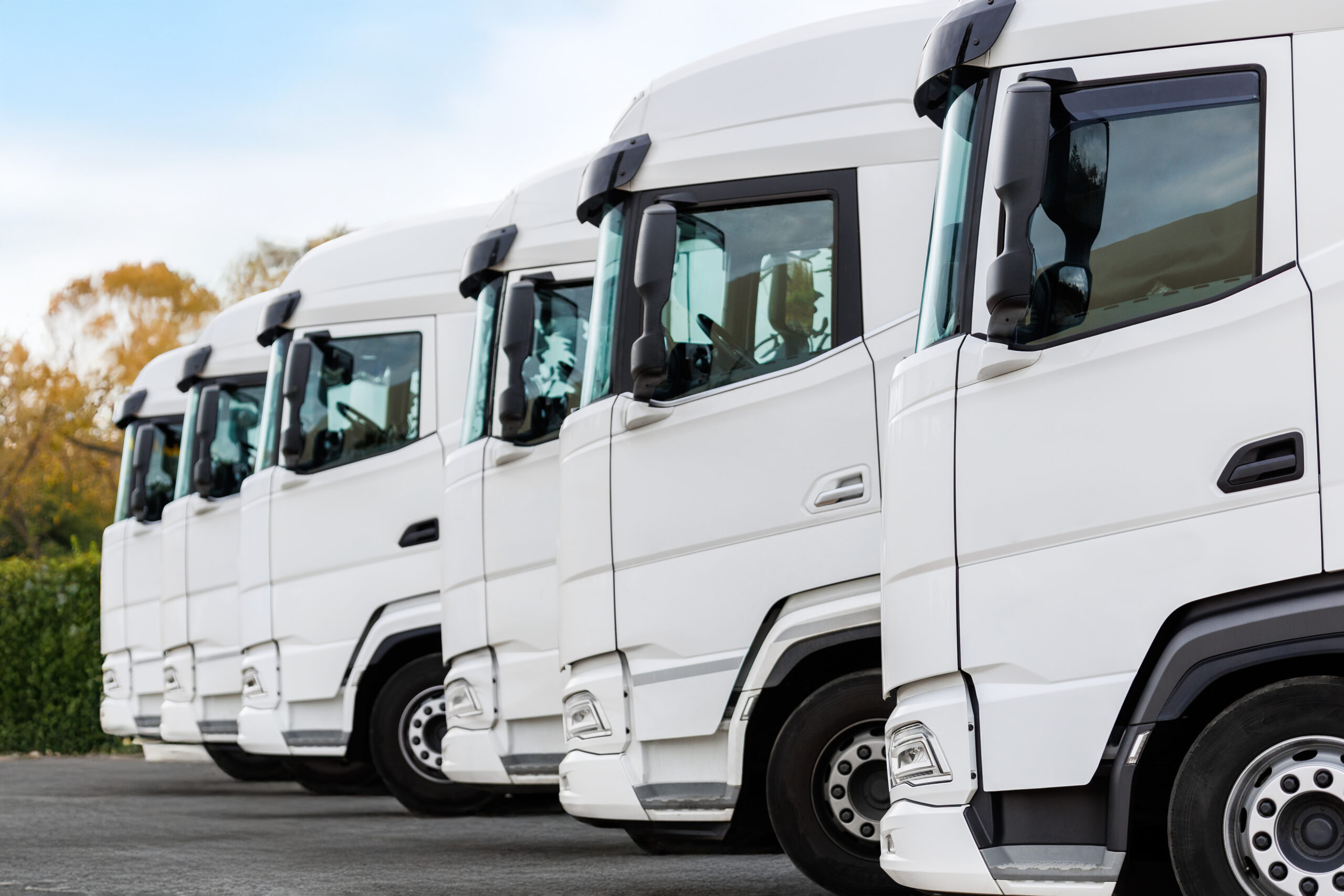 Fleet of new modern electric hybrid hydrogen or diesel white trucks parked in line row outdoors. Cargo freight industrial transportation logistics service. Commercial vehicles maintenance insurance.